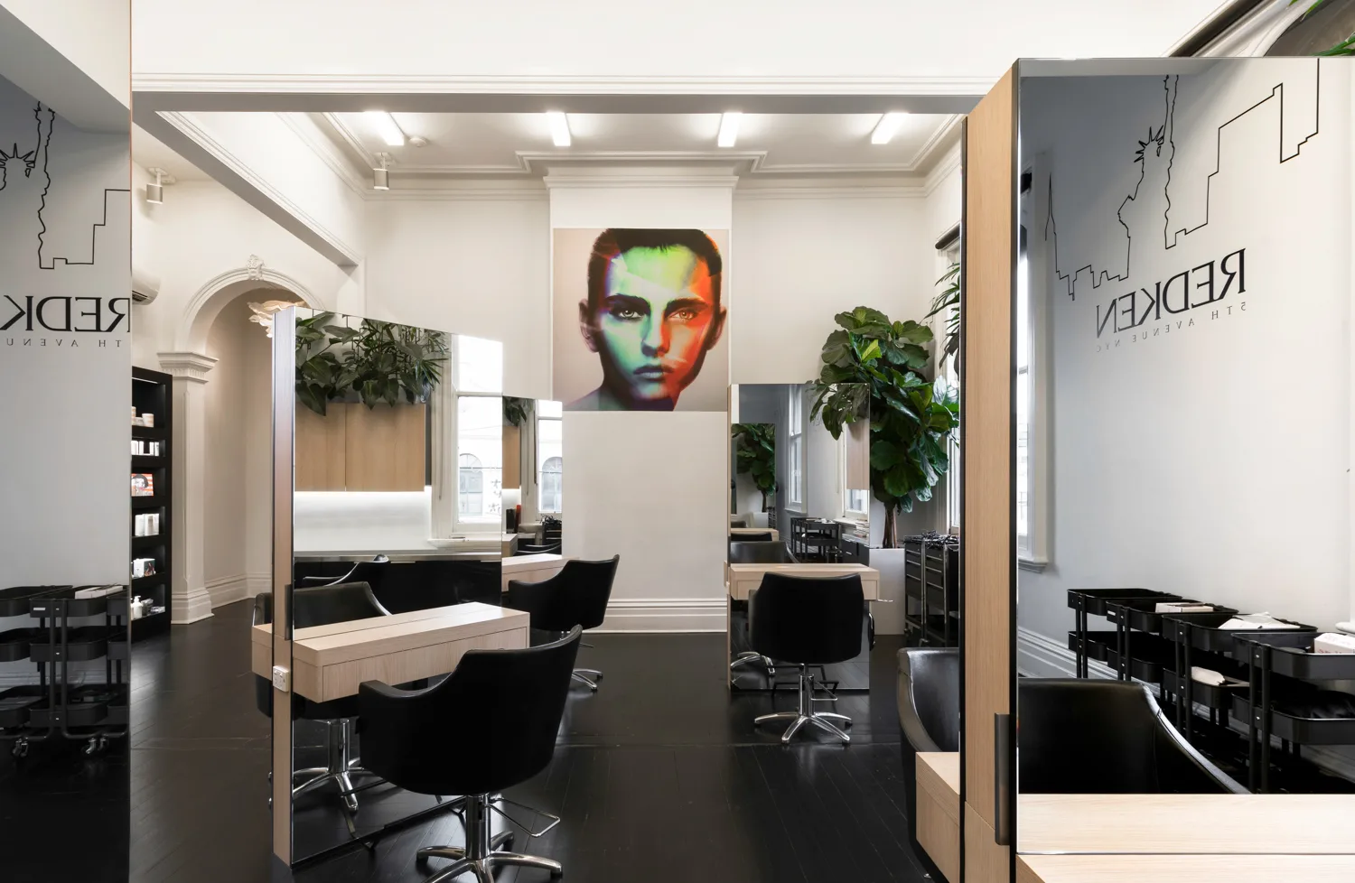 Cream Melbourne salon aisle — mirror stations receding toward the glowing pop-art portrait at the far wall, black timber floors